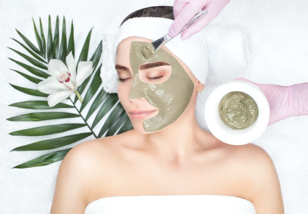The procedure for applying a mask from clay to the face of a beautiful woman. Spa treatments and care of the face in the beauty salon.